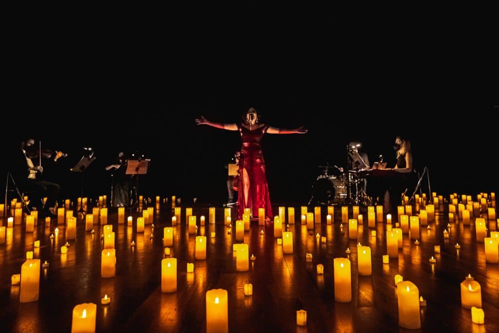 vocalist in red dress singing in front of jaz band surrounded by hundreds of candles