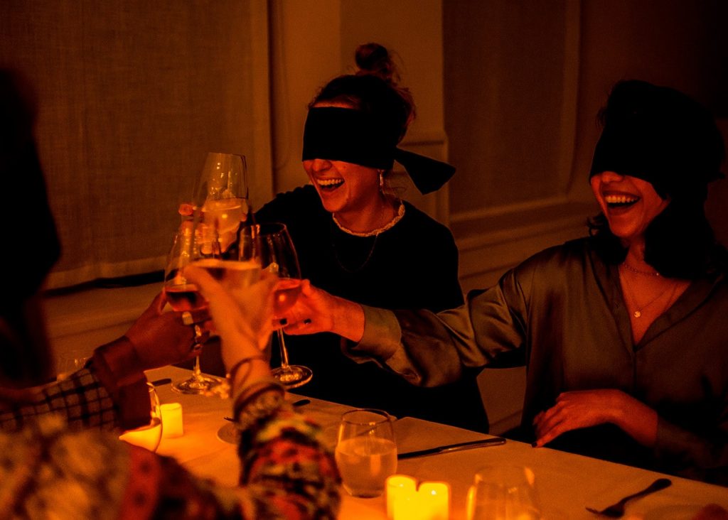 group of young women blindfolded cheering glasses during dining in the dark food experience