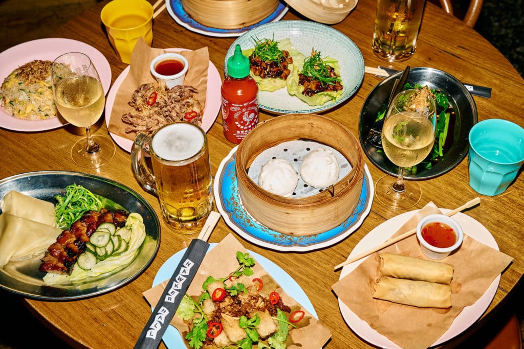 a yum cha feast complete with buns, spring rolls, alcohol and more on a table