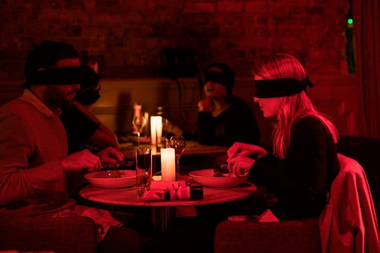 young couple sit blindfolded at dinner during dining in the dark food experience