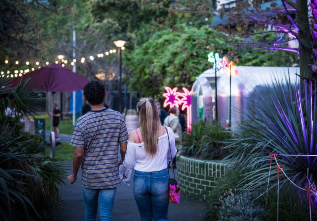 a couple walking through a garden with neon lights in front of them