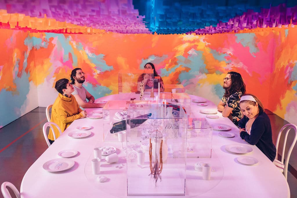 Five people sit around a white table with a brightly coloured wall behind them