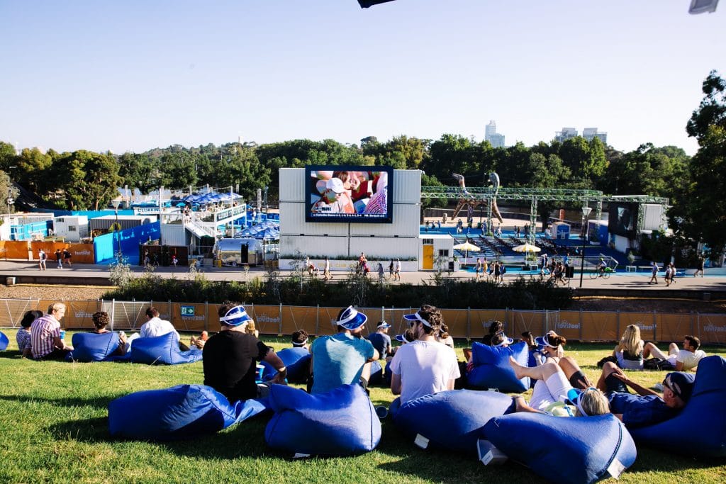 People at the Canadian Club Racquet Club sitting on beanbags on a grassy hilltop, watching the tennis on a big screen
