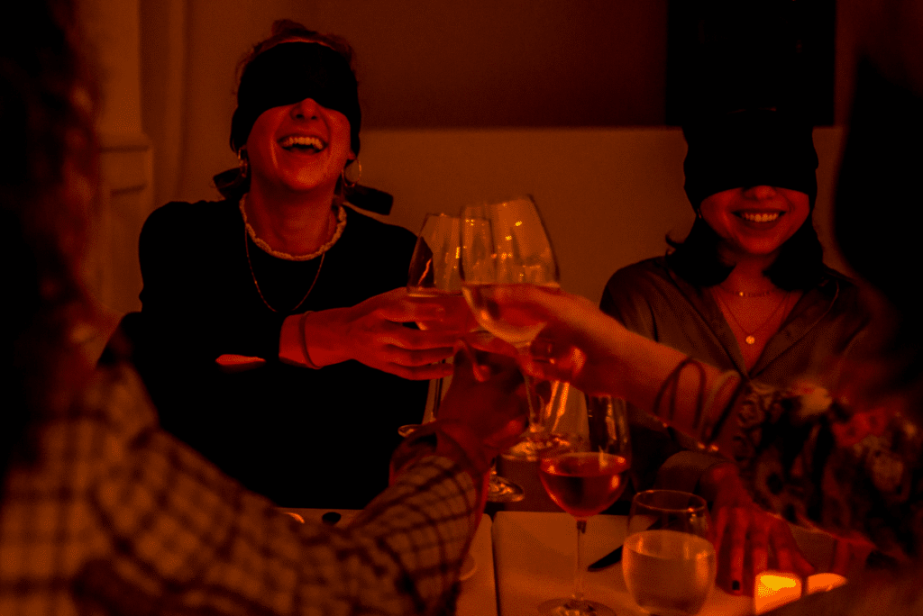 A group of friends laughing and toasting while blindfolded at the Dining in the Dark experience