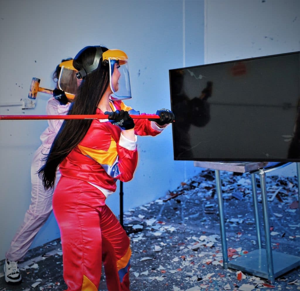 a woman in a red jumpsuit about to hit a tv with a baseball bat