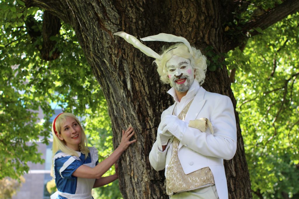Alice holds a tree while a man dressed as White Rabbit looks at the camera