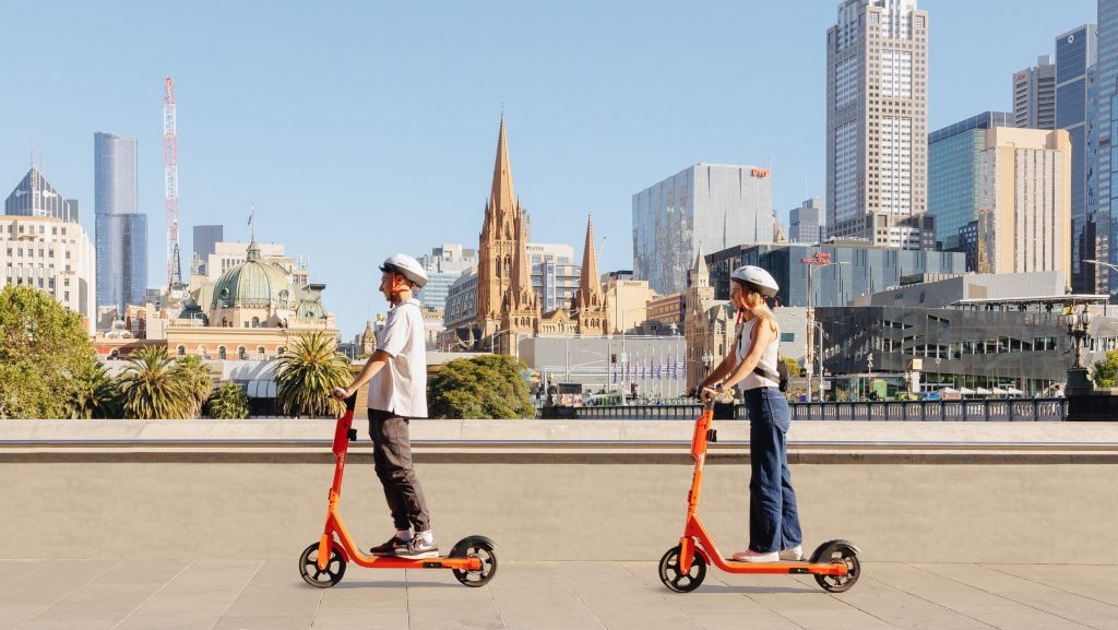 two people riding on orange e-scooters around Melbourne