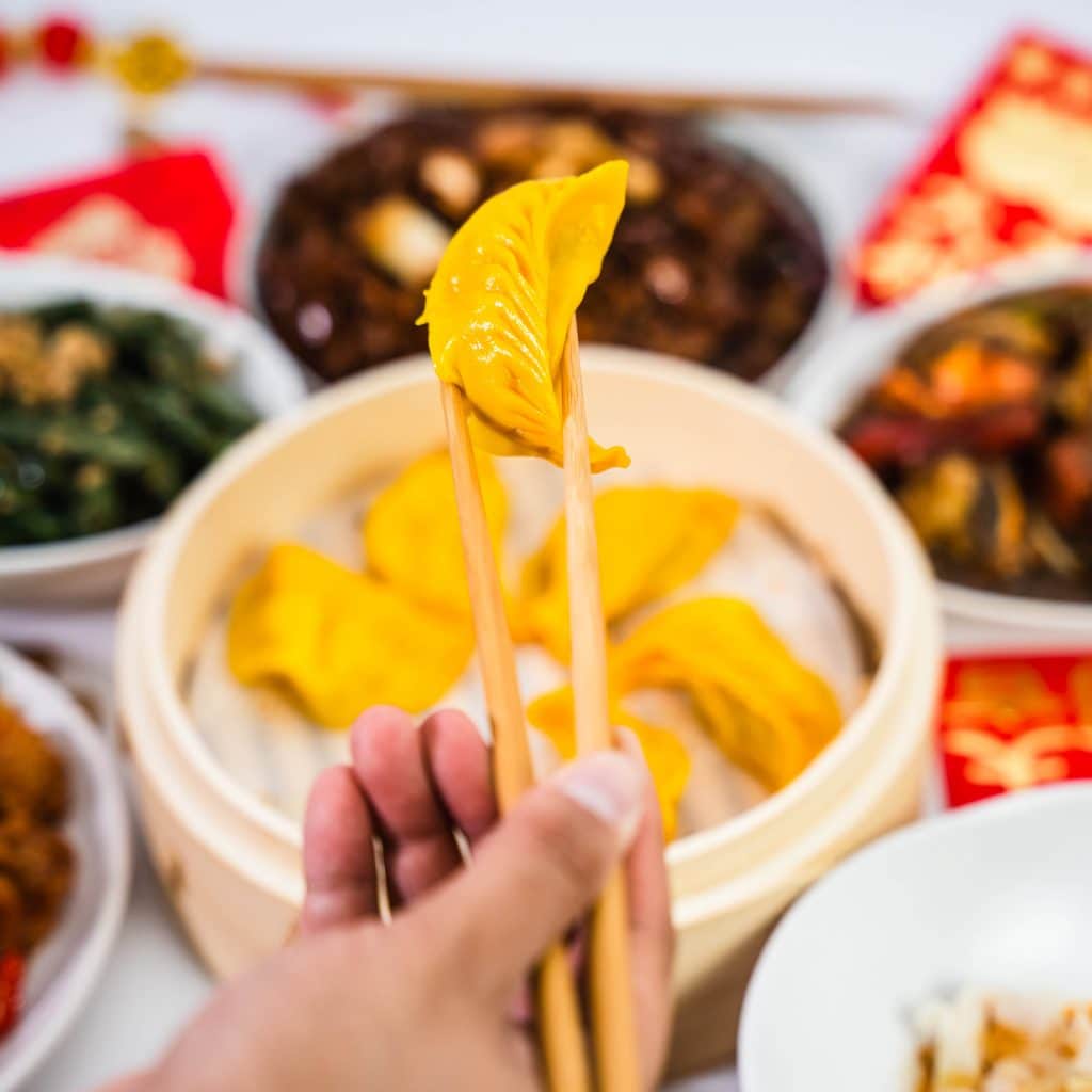 a hand picking up a golden dumpling from a steamer with chopsticks