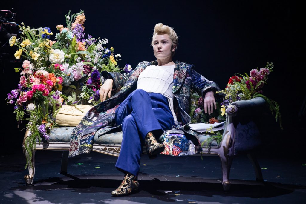 actor sitting down on luxurious sofa surrounded by flowers, dapper dress like Dorian Grey