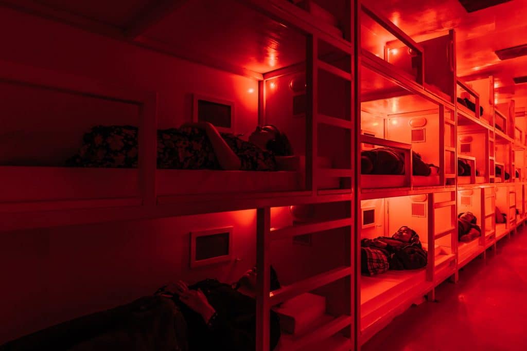 bunk beds three high with red lights as part of coma, darkfield's audio experience in a shipping container
