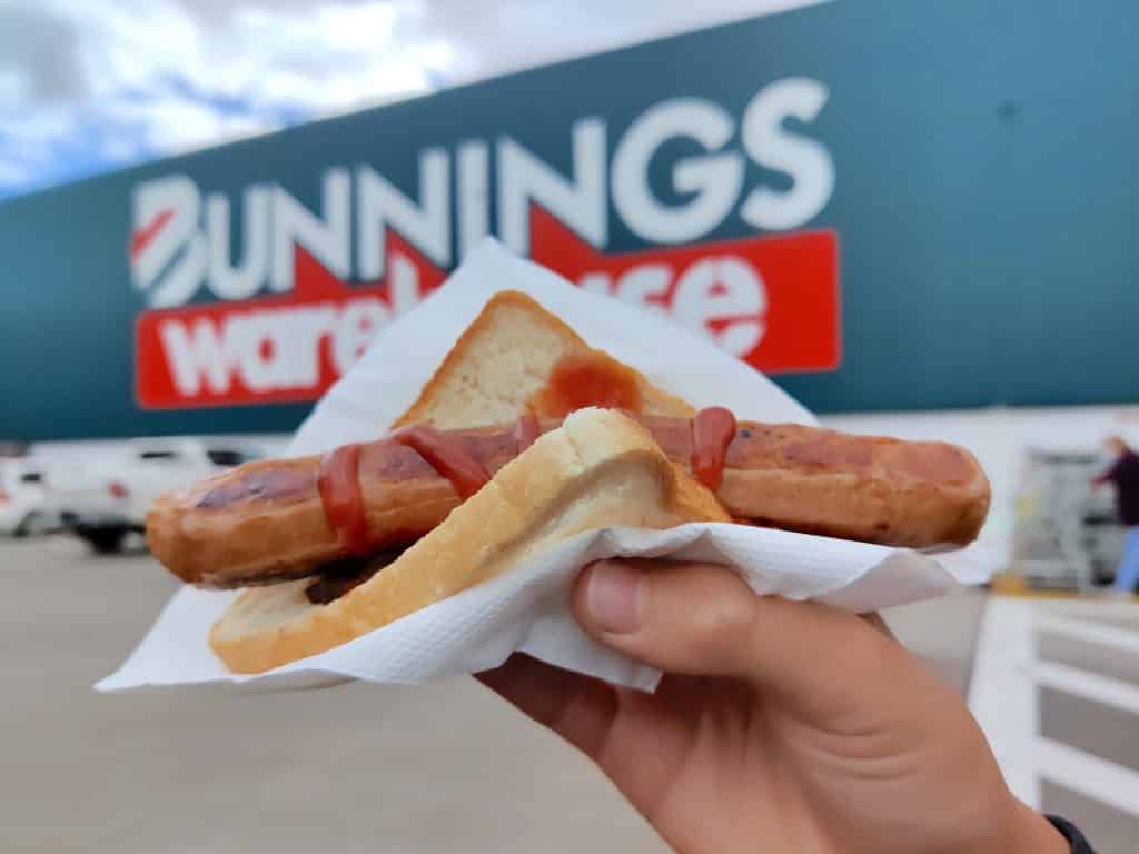 person holding up a snag in front of bunnings store