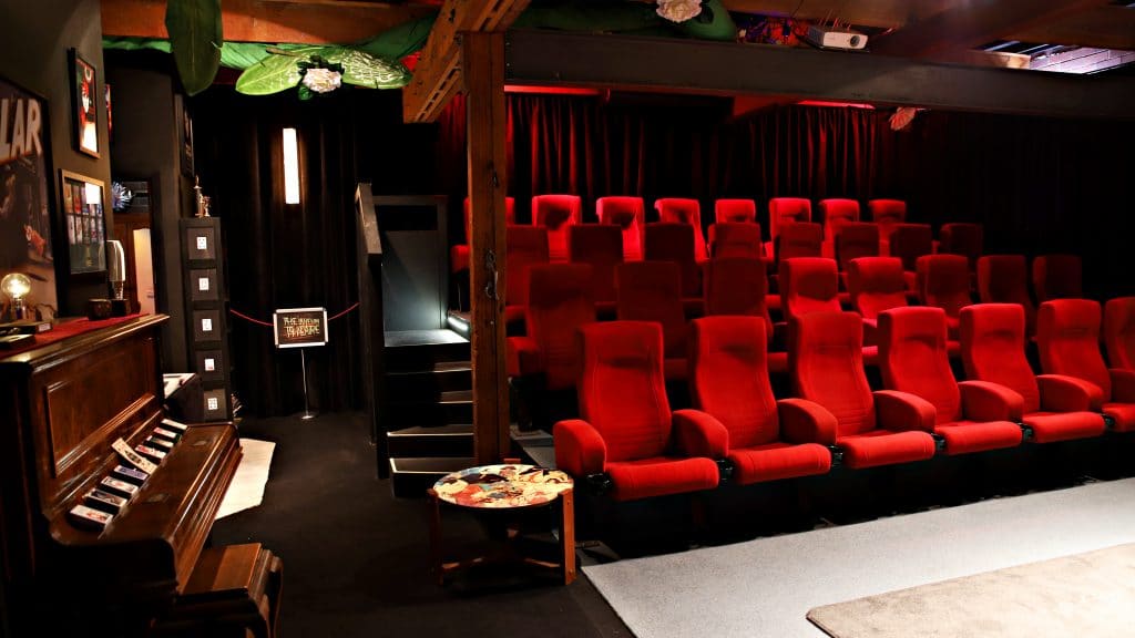 laneway magic theatre, plush red seats on the right like a cinema and magic props on the left, piano, playing cards