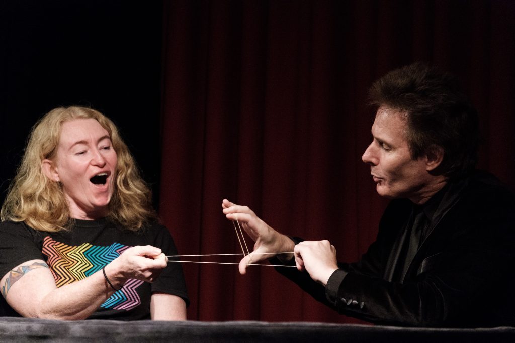 magician tim ellis performing lacky band trick with audience member on stage