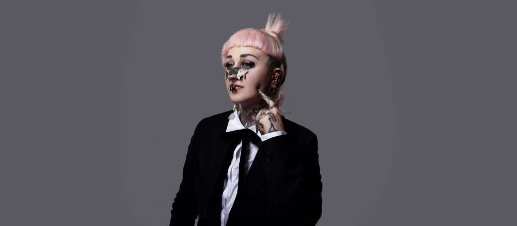 promo shot of frontwoman of Hiatus Kaiyote, Nai Palm, pink hair, silver or metal jewellery on face and fingers