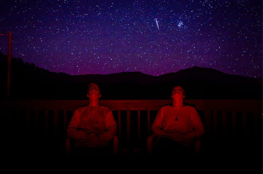 two young men sitting on verandah looking up at night starry sky