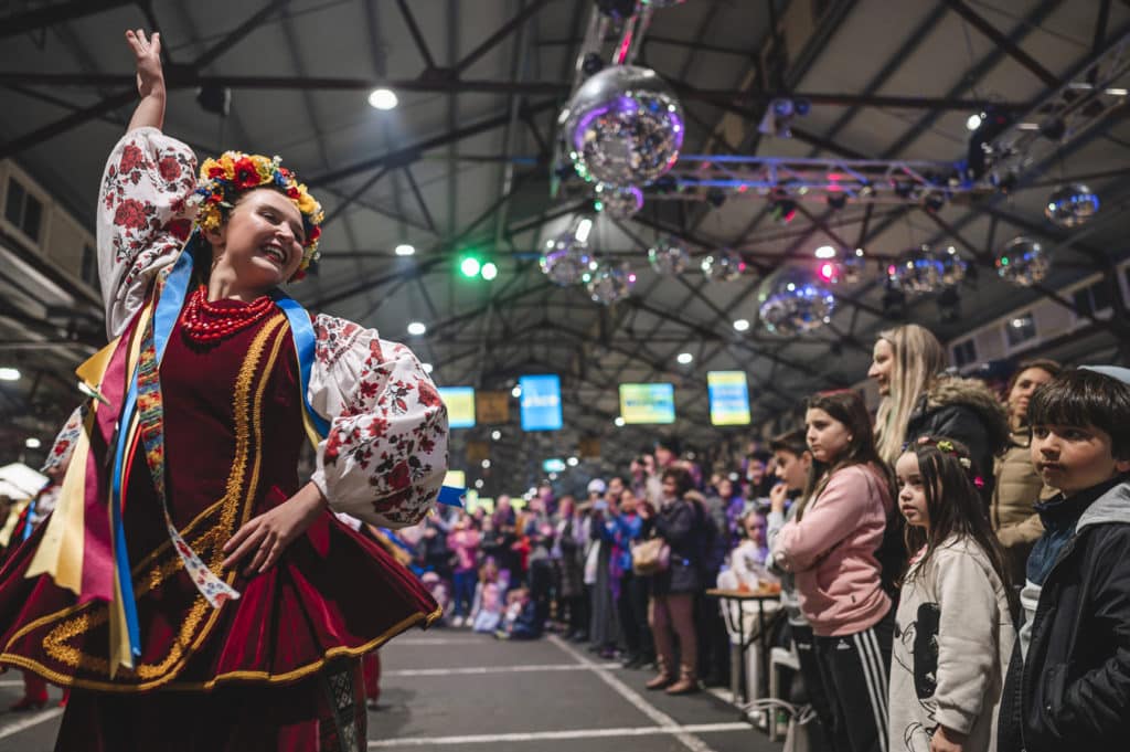 a woman in traditional costume dancing under a disco ball at the Europa Night Market while people watch