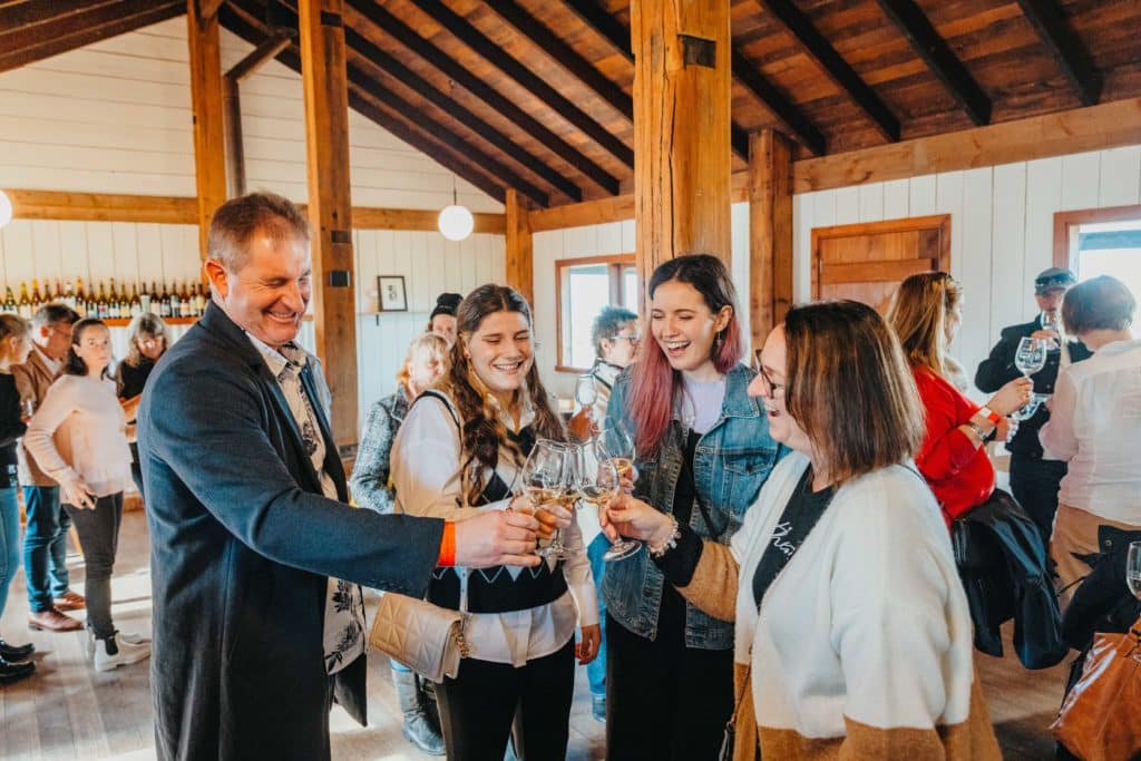 four people clinking their wine glasses together inside a wooden building