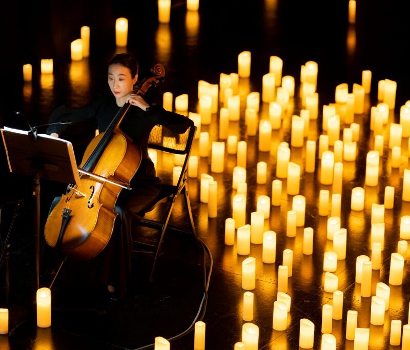 cellist performing at a candlelight concert with hundreds of candles behind her
