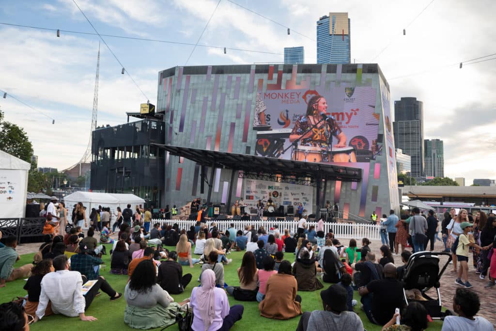 people sitting on a lawn while watching a performance