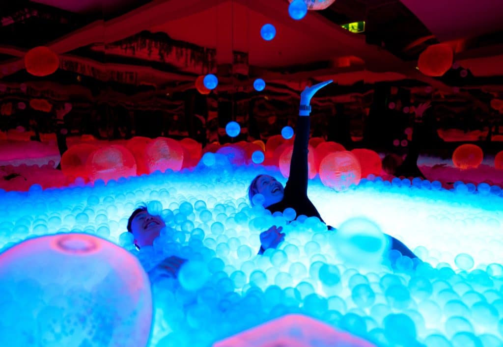 adults playing in a neon-lit ball pit