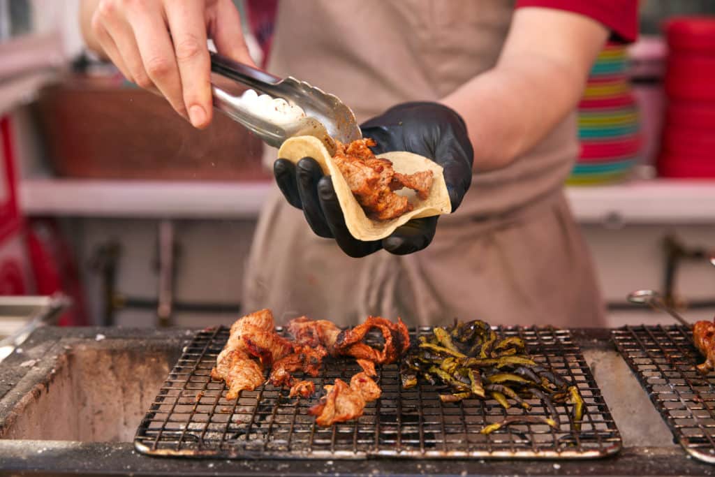 close up of hands using tongs to place meat from a grill into a taco