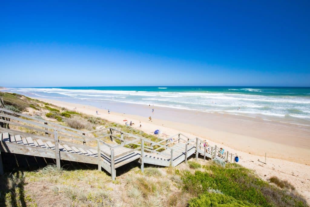 image of thirteenth beach on the bellarine peninsula near melbourne from the top of the wooden stairs showing long stretch of white and golden sand with rolling waves crashing onto the shoreline as far as the eye can see