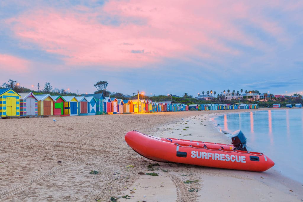 close up of surf rescue dingy on the sand at brighton beach in melbourne with the colourful brighton bathing boxes in the background at dusk, pink fairy floss clouds overhead