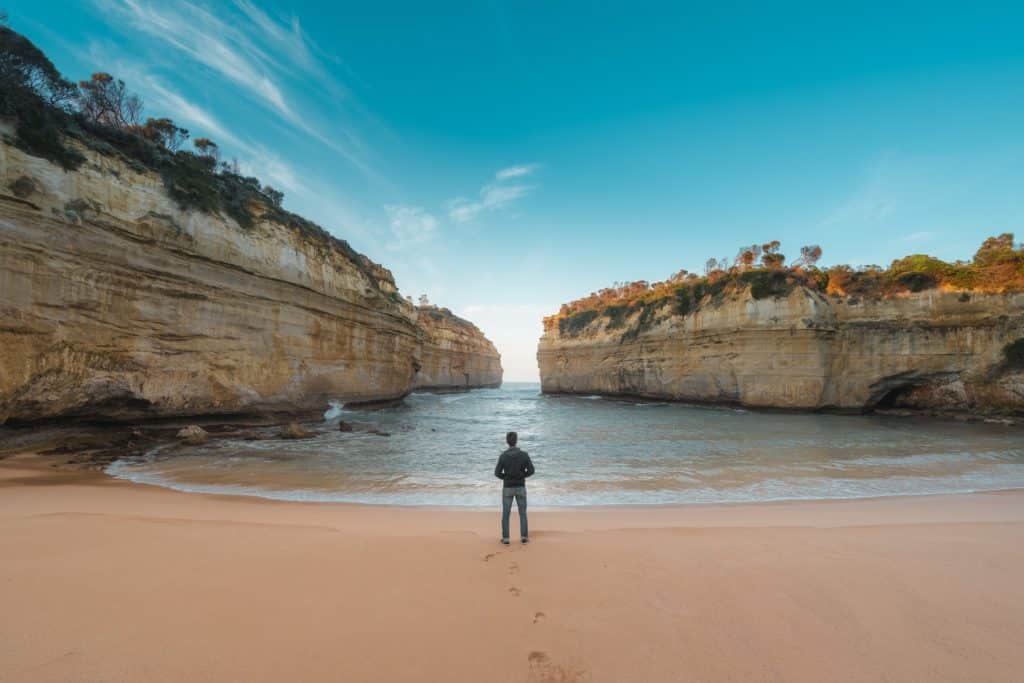 a person standing on the Loch Ard Gorge beach, looking out at the water