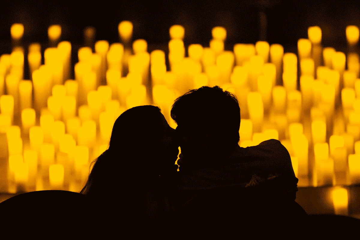 The silhouette of a couple kissing with the glow of hundreds of candles behind them.