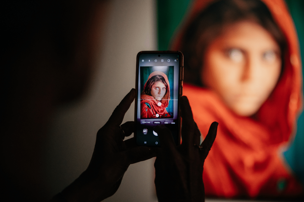 Person taking a photo of the portrait "Afghan Girl" on their phone at the Steve McCurry. ICONS: An Extraordinary Photography Exhibition