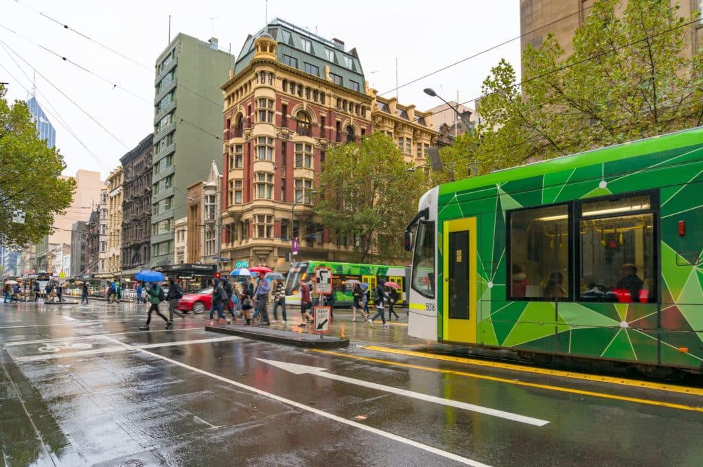 pedestrians with umbrellas cross while a tram waits on a rainy day in Melbourne