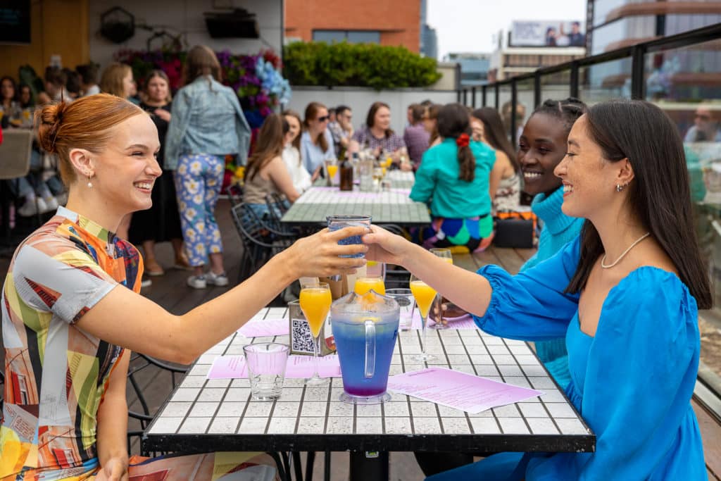 two women clinking their glasses over a blue jug on the rooftop at Harlow Bar