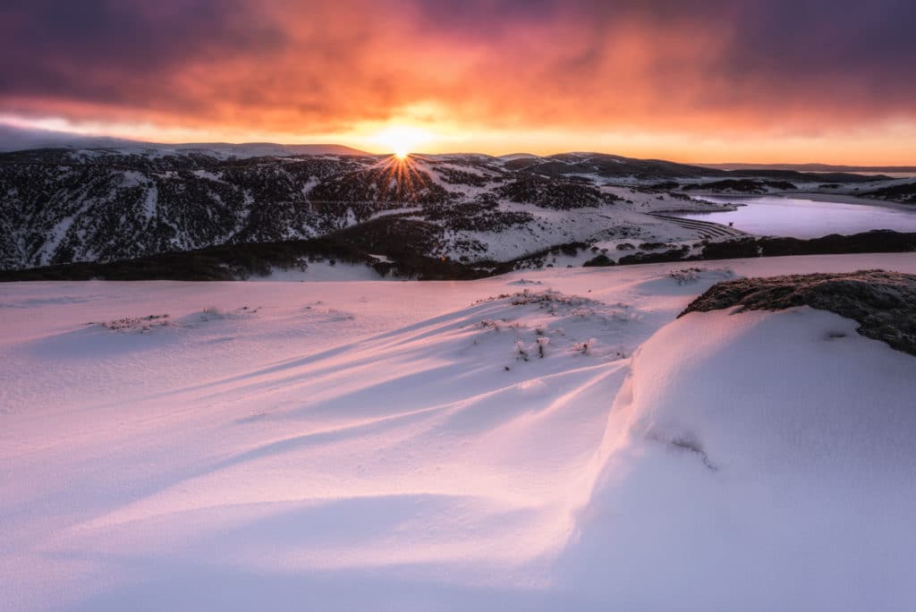 sunrise over a distant mountain range and a blanket of snow on Falls Creek in Victoria