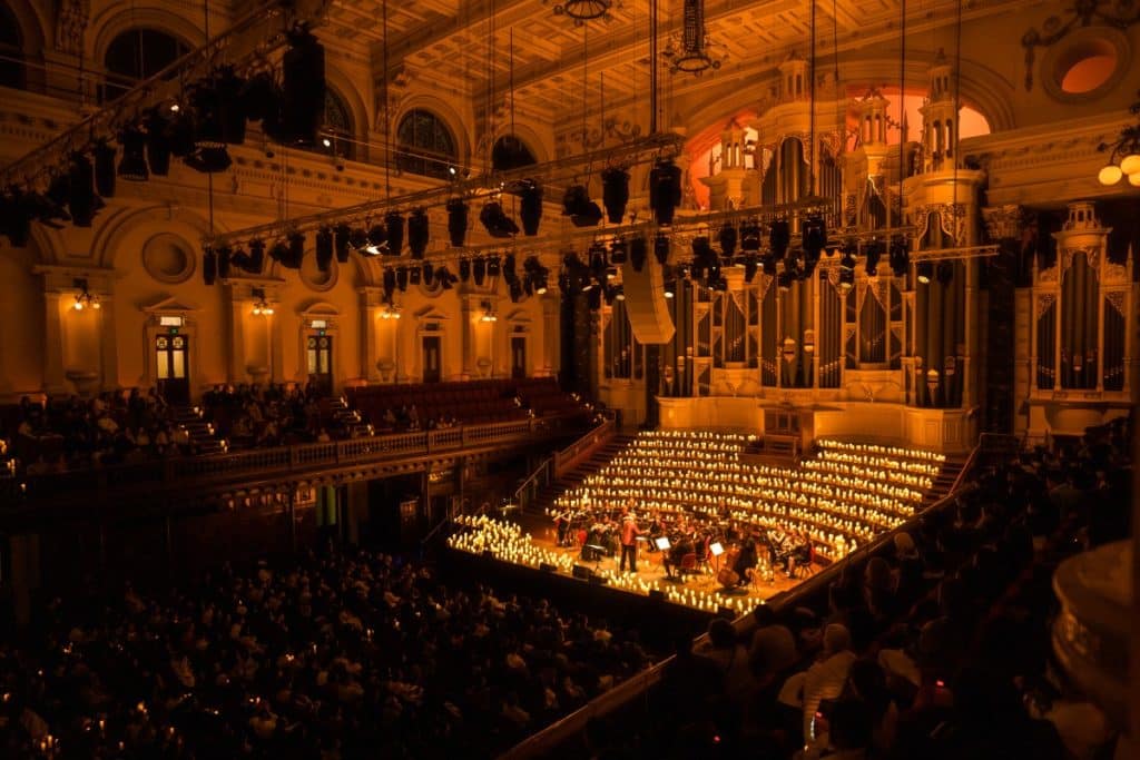 A wide shot of an orchestra performing in an auditorium completely bathed in candlelight