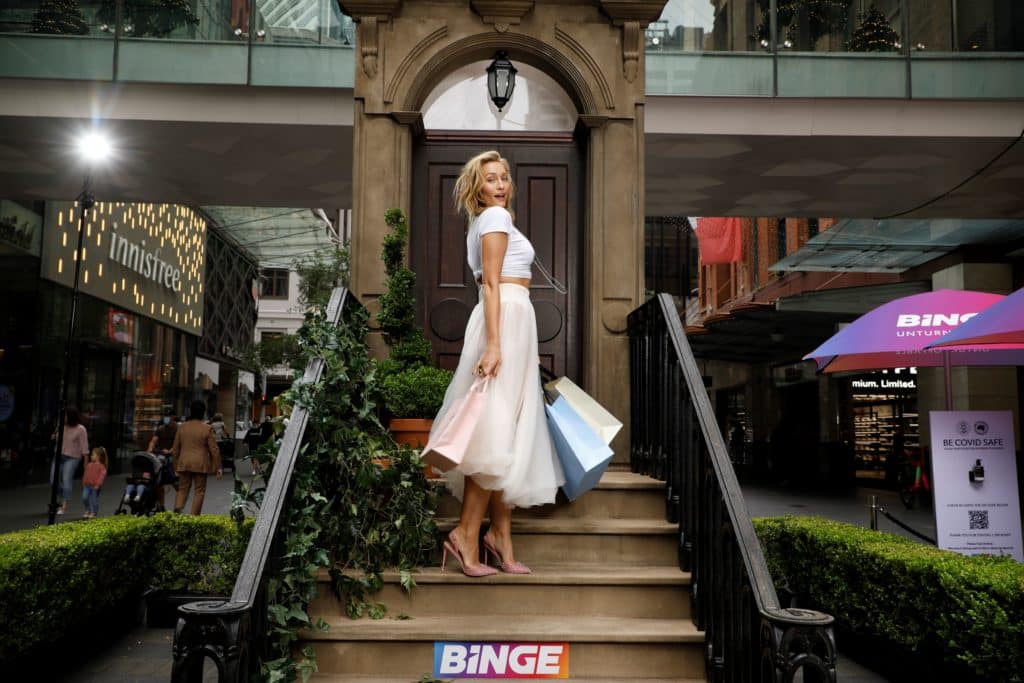 a woman holding shopping bags posing on a replica of Carrie Bradshaw's apartment stoop