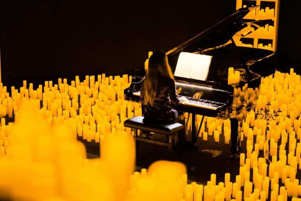 A back shot of a pianist playing the grand piano surrounded by hundreds of candles