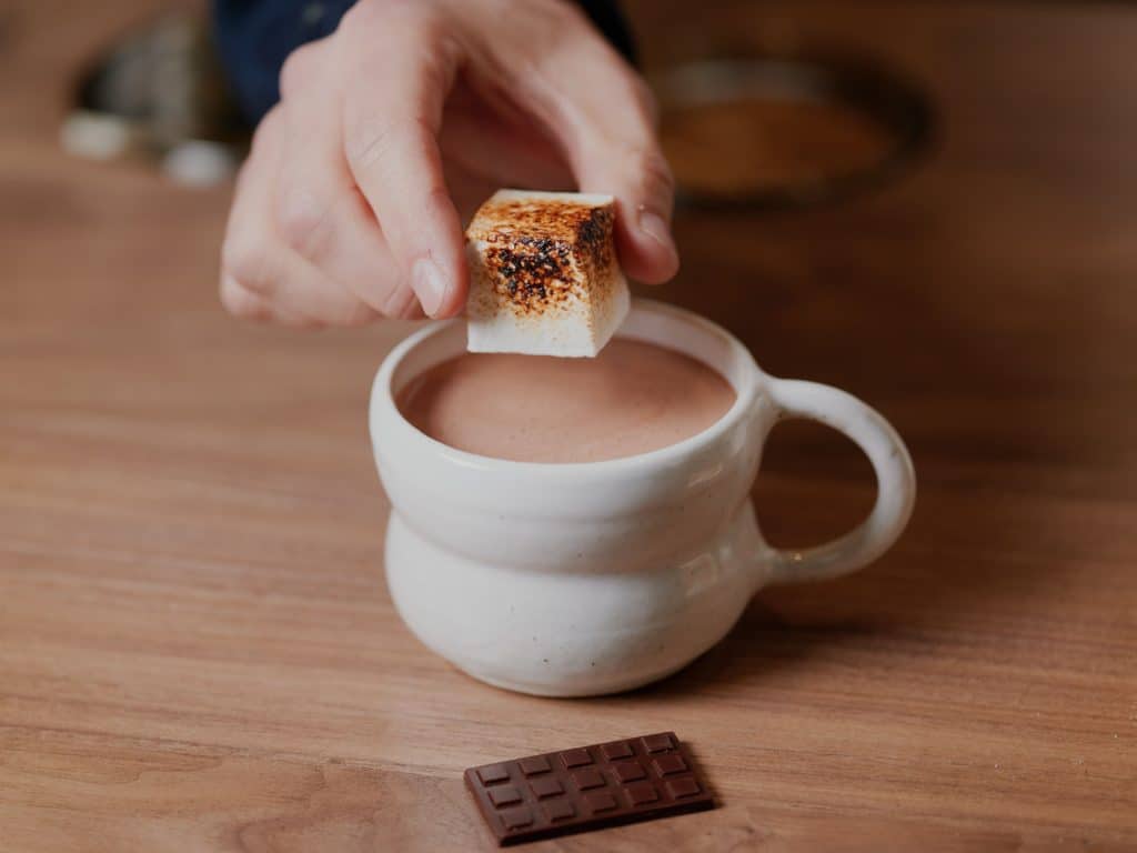 a hand holding a marshmallow above a cup of hot chocolate at a store in Melbourne