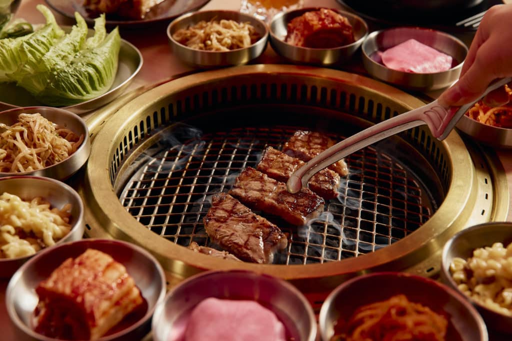 someone barbequing beef at Mansae, one of the Korean restaurants in Melbourne. The grill is surrounded by side dishes like kimchi and lettuce