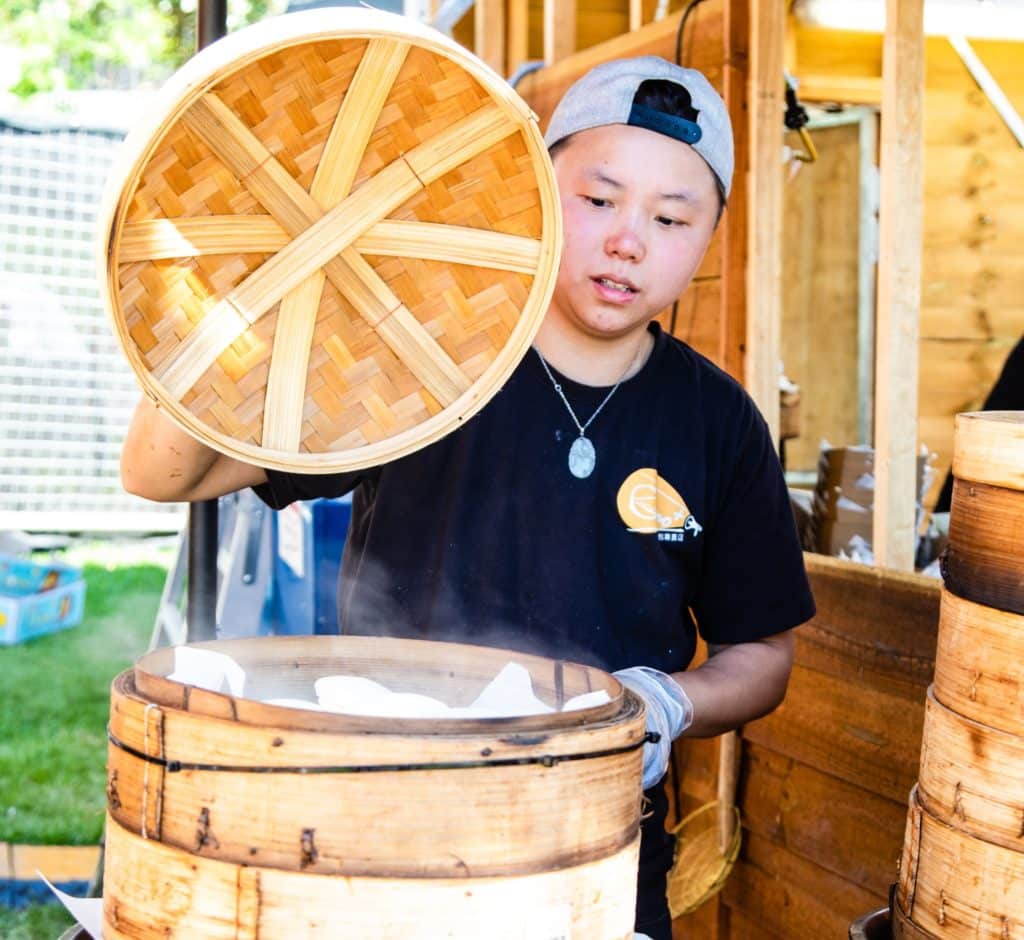 a cook opening up a steam basket to reveal dumplings inside
