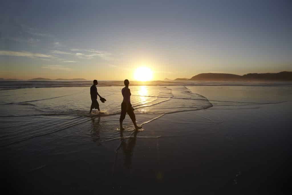 a couple walking along Squeaky Beach at sunset