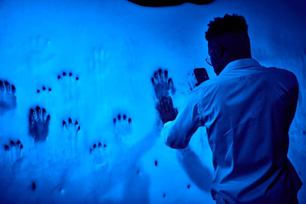 man touching iceberg gallery wall, which is covered in handprints