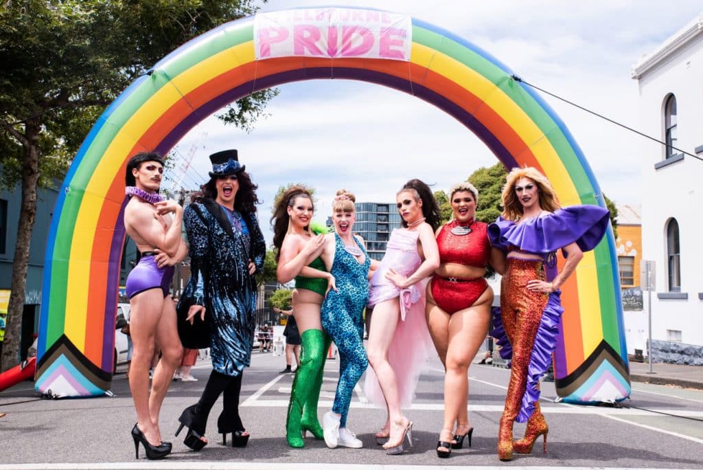 seven people dressed in bright colours in front of a rainbow for Victoria's Pride