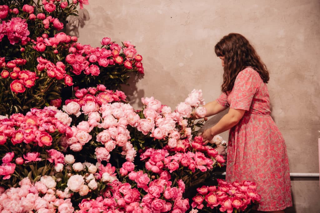 a woman picking up a bunch of peonies at the Peony Party by Hello Blooms