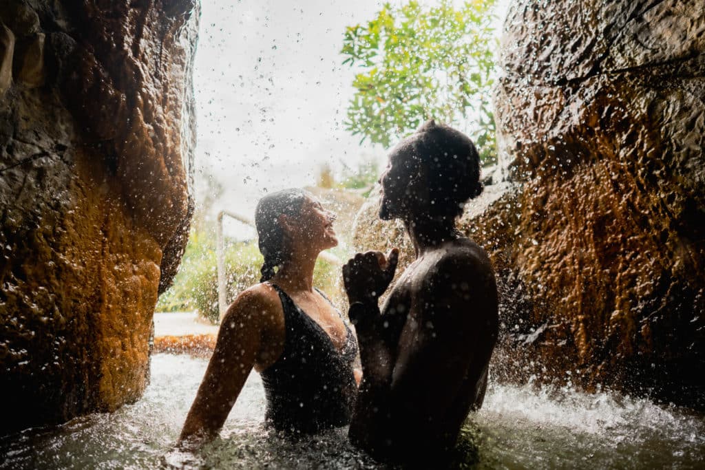 a couple under a waterfall at Deep Blue Hot Springs