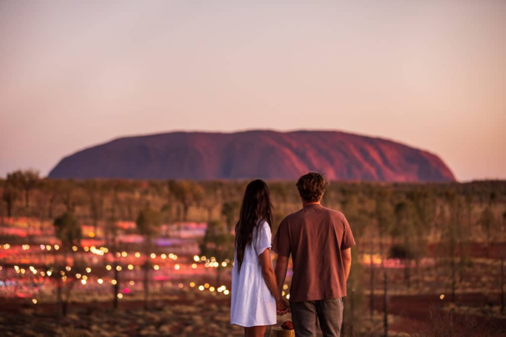 a couple looking at Uluru and the Field of Light installation, which you can see by taking a flight with Virgin Australia